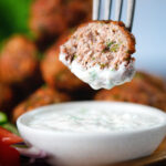 Cut open fried Greek meatballs or keftedes dipped in a garlic yoghurt sauce.