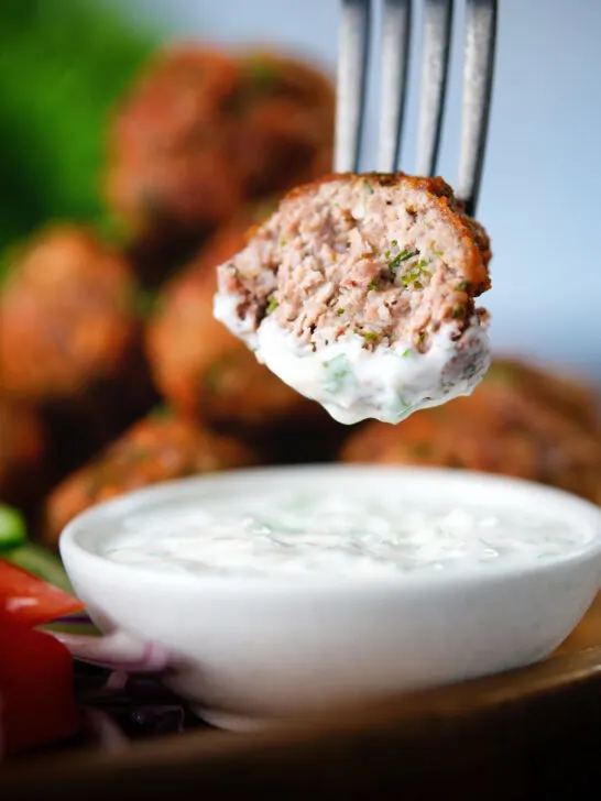 Cut open fried Greek meatballs or keftedes dipped in a garlic yoghurt sauce.