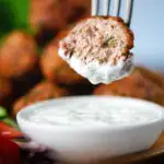 Cut open fried Greek meatballs or keftedes dipped in a garlic yoghurt sauce.