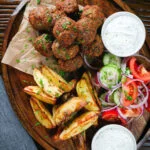 Overhead Greek meatballs, keftedes served with a yoghurt dip, salad and potato wedges.