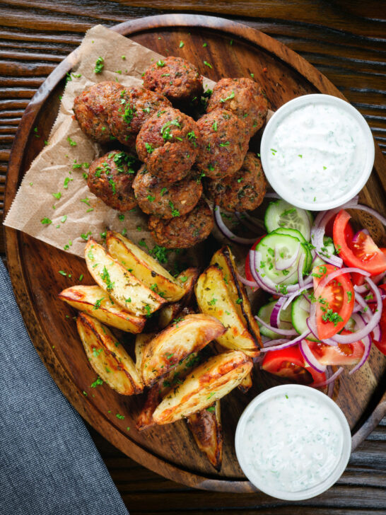 Overhead Greek meatballs, keftedes served with a yoghurt dip, salad and potato wedges.