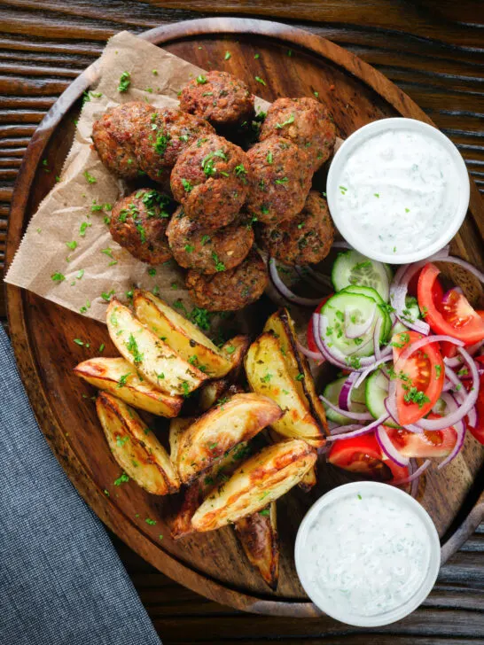 Overhead Greek meatballs, keftedes served with a yoghurt dip, salad and potato wedges.