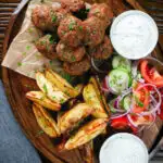 Overhead Greek meatballs, keftedes served with a yoghurt dip, salad and potato wedges.