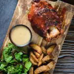 Overhead crispy roast ham hock glazed with honey and mustard served with potato wedges and cider sauce.