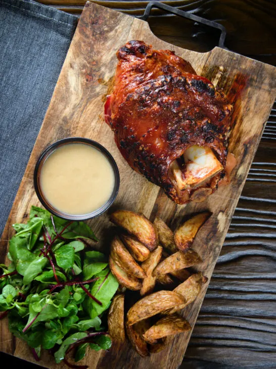 Overhead crispy roast ham hock glazed with honey and mustard served with potato wedges and cider sauce.