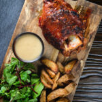 Overhead crispy roast ham hock glazed with honey and mustard served with potato wedges and cider sauce.