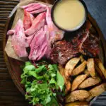 Overhead roast ham hock meat served with potato wedges and cider sauce.