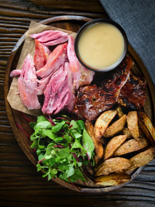 Overhead roast ham hock meat served with potato wedges and cider sauce.