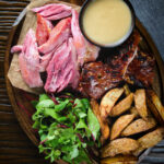 Overhead roast ham hock meat served with potato wedges and cider sauce.