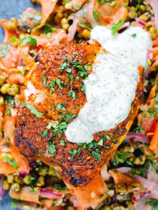 Overhead close-up tandoori cod fish with raita and a mung bean salad.