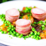 Oven Baked bacon wrapped pork tenderloin, crushed roasted potatoes, braised chicory and peas.