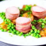 Oven Baked bacon wrapped pork tenderloin, crushed roasted potatoes, braised chicory and peas.
