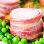 Close-up bacon wrapped pork tenderloin, crushed roasted potatoes, braised chicory and peas.