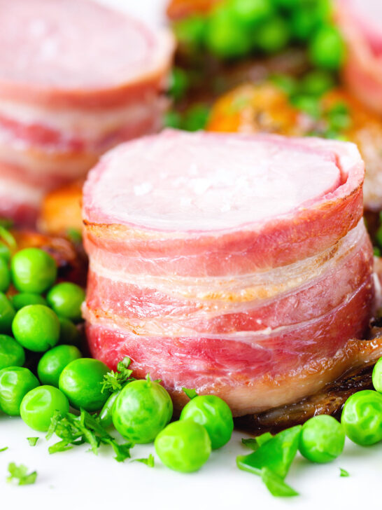 Close-up bacon wrapped pork tenderloin, crushed roasted potatoes, braised chicory and peas.