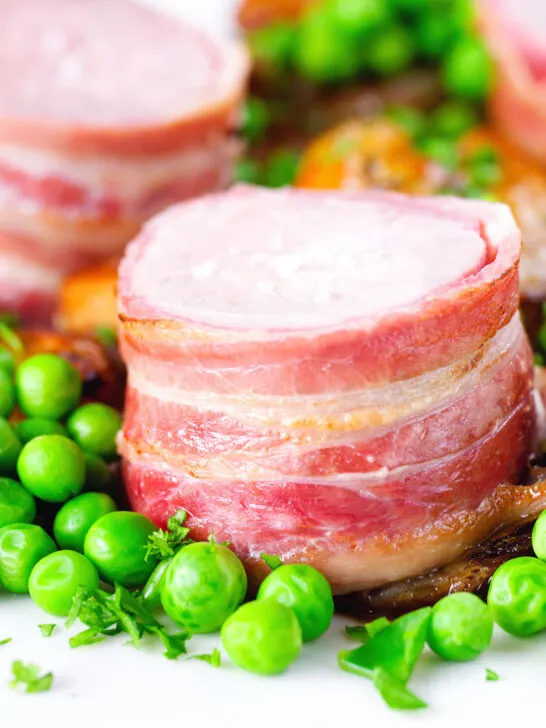 Close-up bacon wrapped pork tenderloin, crushed roasted potatoes, braised chicory and peas.