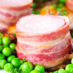Close-up bacon wrapped pork tenderloin, crushed roasted potatoes, braised chicory and peas.