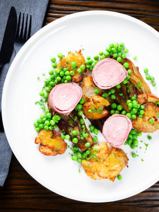 Overhead bacon wrapped pork tenderloin, crushed roasted potatoes, braised chicory and peas.