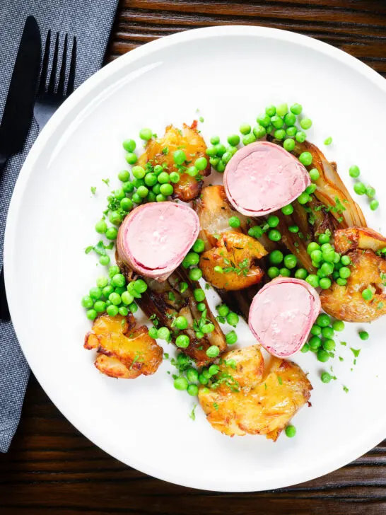 Overhead bacon wrapped pork tenderloin, crushed roasted potatoes, braised chicory and peas.