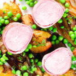 Overhead close-up bacon wrapped pork tenderloin, crushed roasted potatoes, braised chicory and peas.