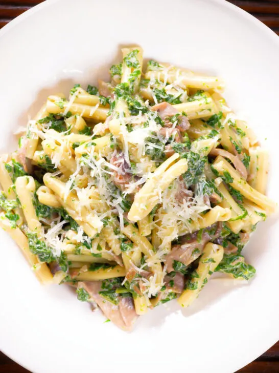 Overhead close-up spinach and mushroom pasta with parmesan cheese.