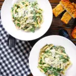 Overhead spinach and mushroom pasta with parmesan cheese and garlic bread.