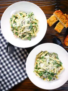 Overhead spinach and mushroom pasta with parmesan cheese and garlic bread.