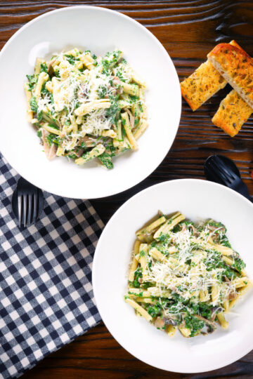 Overhead spinach and mushroom pasta with parmesan cheese and garlic bread.