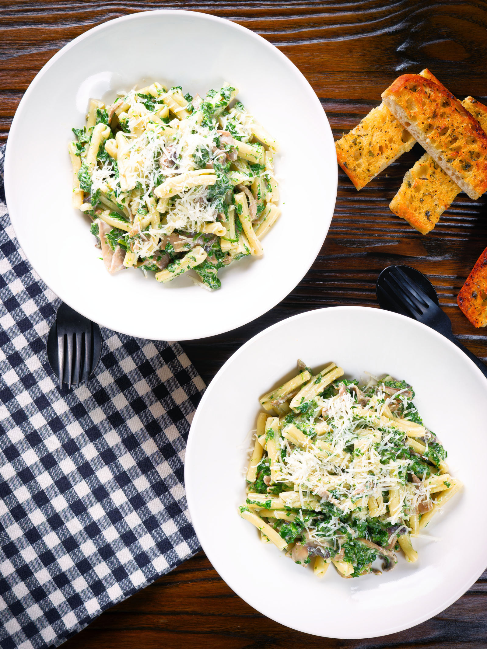 Overhead spinach and mushroom pasta with parmesan cheese and garlic bread.