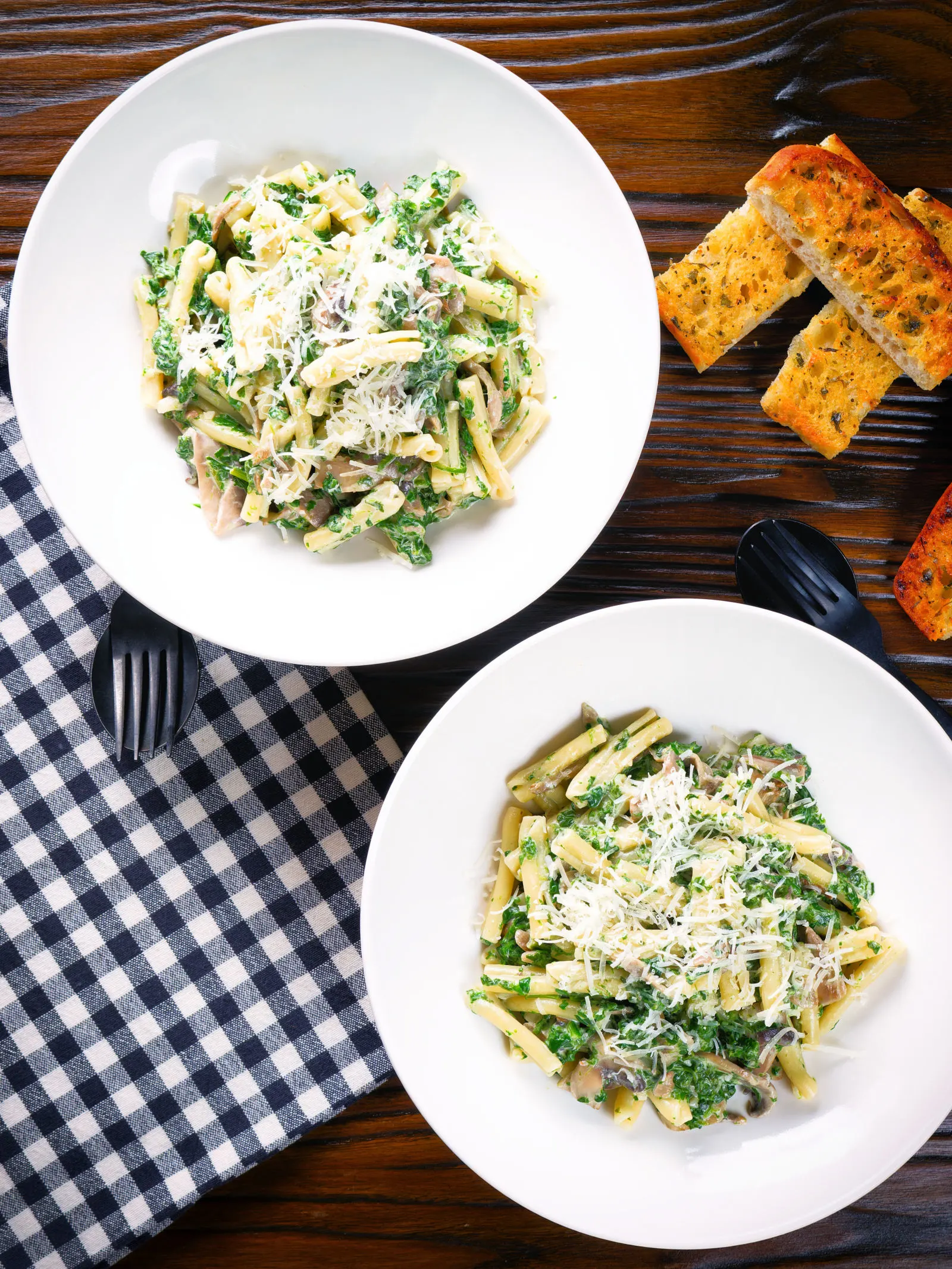 Overhead spinach and mushroom pasta with parmesan cheese and garlic bread.