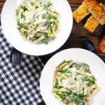 Overhead spinach and mushroom pasta with parmesan cheese and garlic bread.