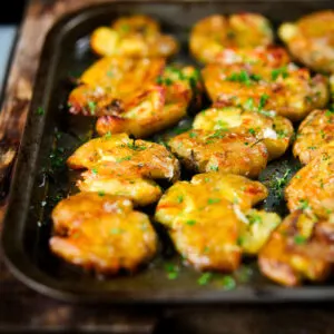 Crispy crushed (or smashed) herb roasted new potatoes in a roasting tin.
