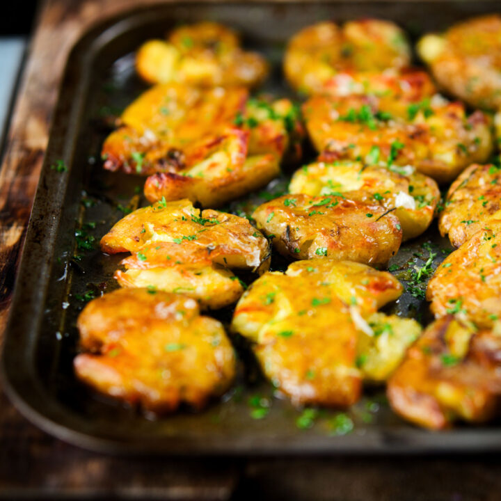 Crispy crushed (or smashed) herb roasted new potatoes in a roasting tin.