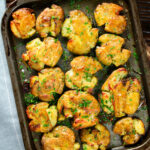 Overhead crispy roasted crushed (smashed) new potatoes on a roasting tray.