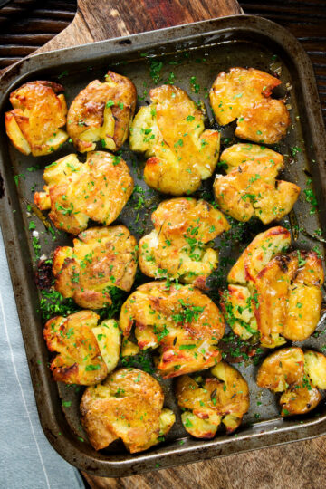 Overhead crispy roasted crushed (smashed) new potatoes on a roasting tray.