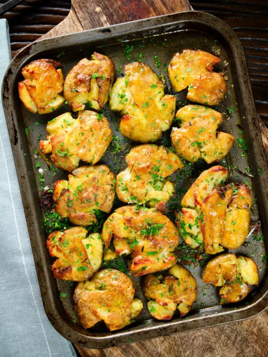 Overhead crispy roasted crushed (smashed) new potatoes on a roasting tray.