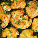 Overhead close-up crispy roasted crushed (smashed) new potatoes on a roasting tray.