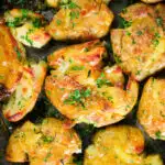 Overhead close-up crispy roasted crushed (smashed) new potatoes on a roasting tray.