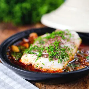Cod fish tagine with preserved lemons garnished with sumac and parsley.