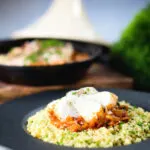 Flaked cod fish tagine served with buttered couscous with a traditional cooking pot in the background.