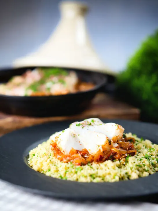Flaked cod fish tagine served with buttered couscous with a traditional cooking pot in the background.