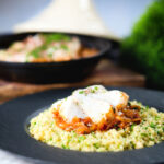 Flaked cod fish tagine served with buttered couscous with a traditional cooking pot in the background.