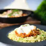 Flaked cod fish tagine served with buttered couscous with a traditional cooking pot in the background.