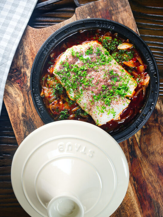 Overhead cod fish tagine with preserved lemons, harissa and sumac in a traditional pot.