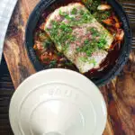Overhead cod fish tagine with preserved lemons, harissa and sumac in a traditional pot.