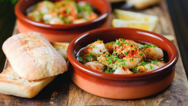 Spanish gambas pil pil spicy chilli and garlic prawns served with bread, parsley and lemons.