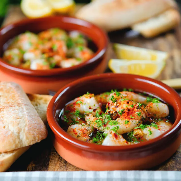Spanish gambas pil pil spicy chilli and garlic prawns served with bread, parsley and lemons.