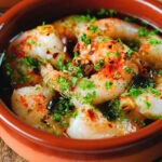 Close-up Spanish gambas (prawns) pil pil served with fresh parsley, bread and lemon wedges.