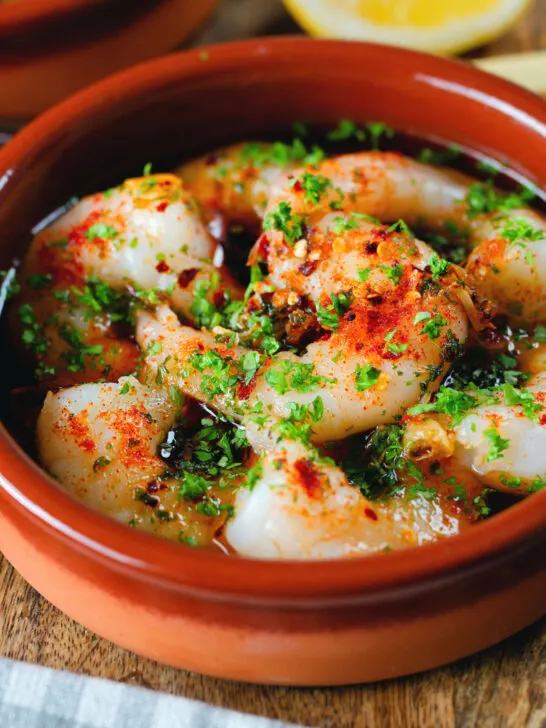 Close-up Spanish gambas (prawns) pil pil served with fresh parsley, bread and lemon wedges.