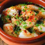 Close-up Spanish gambas (prawns) pil pil served with fresh parsley, bread and lemon wedges.