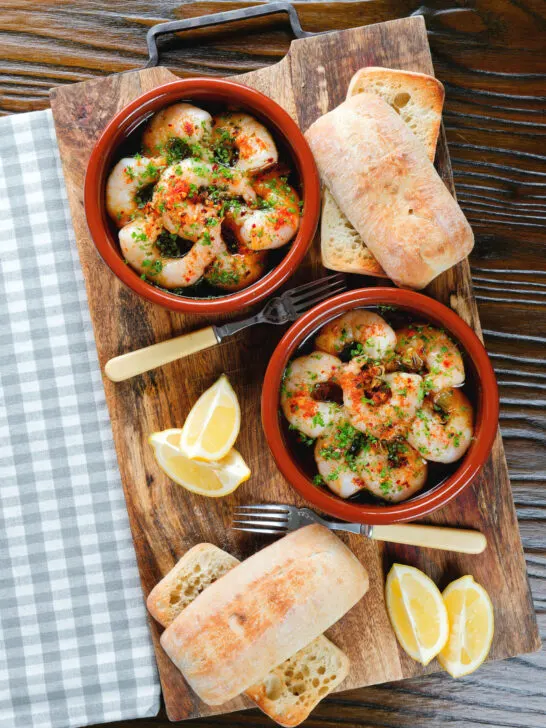 Overhead Spanish gambas (prawns) pil pil served with fresh parsley, bread and lemon wedges.